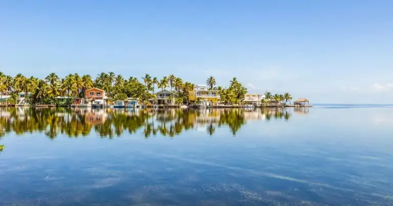 Casas con palmeras reflejadas en agua calmada sobre un arrecife
