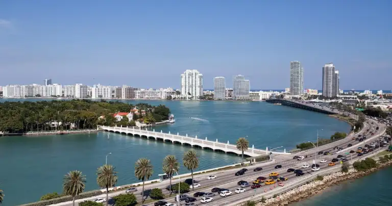 Vista aérea de Miami, mostrando un puente, la carretera y edificios altos a lo lejos. La imagen captura el contraste entre el agua y la ciudad.