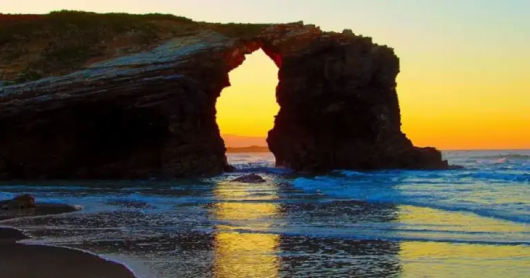 Arcos de piedra natural en playa al atardecer con mar