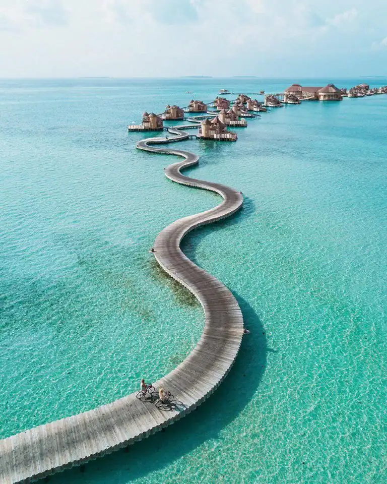 Pasarela serpentante sobre agua turquesa conectando bungalós