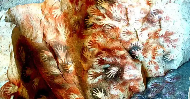 Pared rocosa con marcas y siluetas de manos rojas