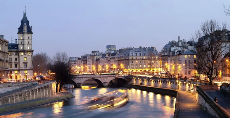 Puente iluminado sobre río con edificios parisinos al anochecer