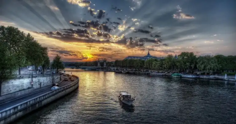 Río al atardecer con barcazas y árboles a la orilla