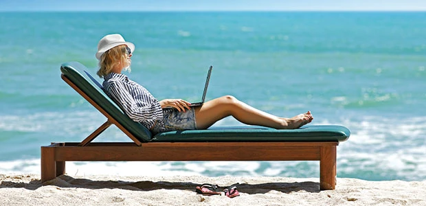 Persona trabajando en laptop desde una tumbona en la playa