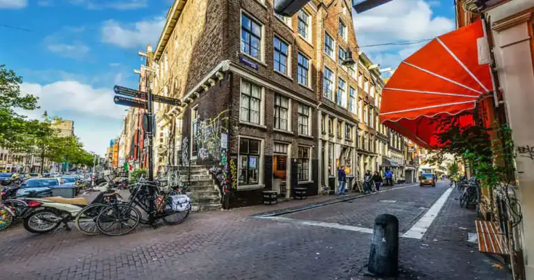 Calle adoquinada del Barrio Rojo de Ámsterdam con edificios históricos y sombrilla roja