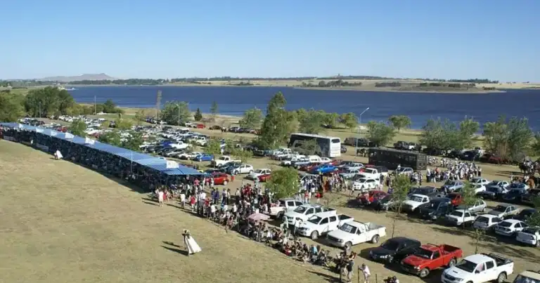Vista aérea de una fiesta con multitud de visitantes, autos estacionados y un escenario azul