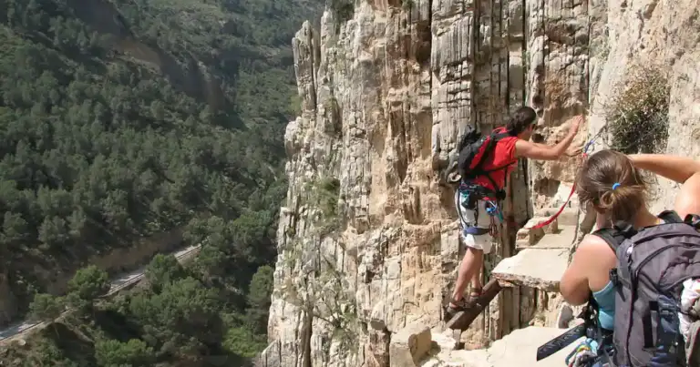 Escaladores practicando rappel en una empinada pared de roca con valles boscosos al fondo