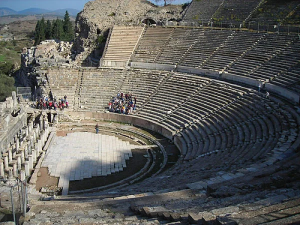 Anfiteatro de piedra semicircular con gradas y turistas en la arena
