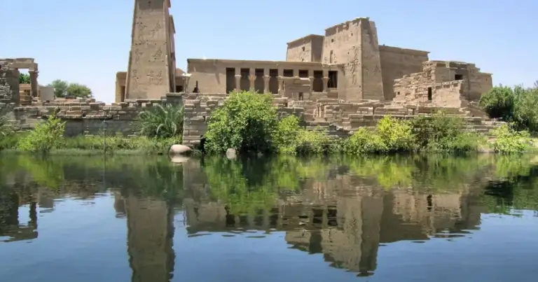 Ruinas de templo antiguo de piedra junto a un río con palmeras