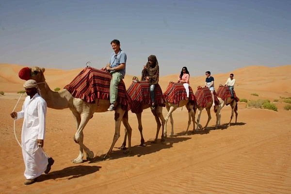 Grupo de turistas cabalgando en camellos por dunas de arena