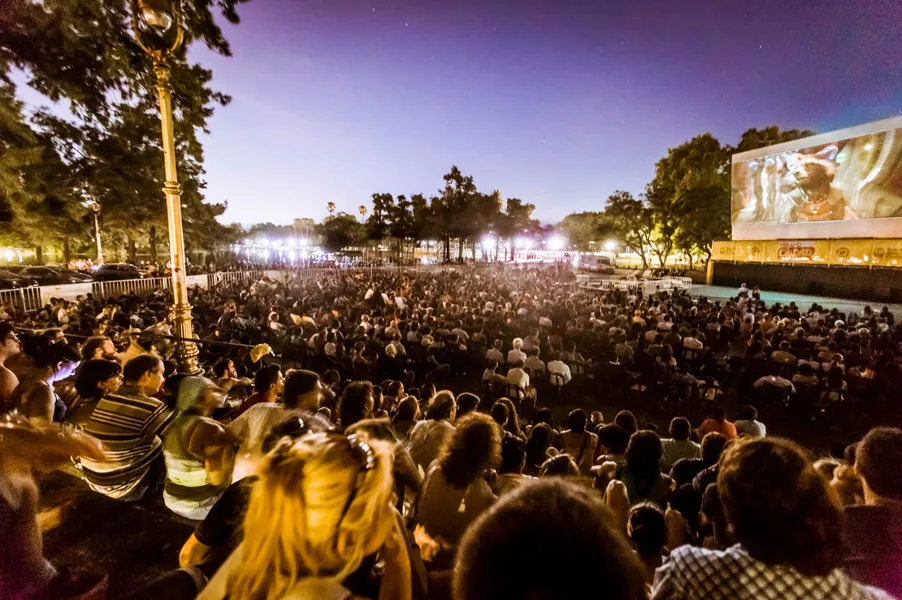Autocine de noche con pantalla gigante y público en vehículos