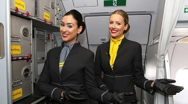 Dos azafatas en uniforme azul dentro de cabina de avión