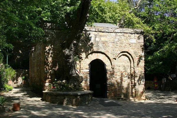 Capilla antigua de piedra con arcos decorativos bajo árboles frondosos
