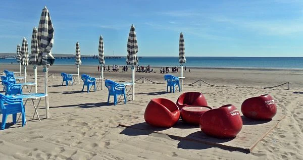 Playa arenosa con sombrillas y sillas azules en Puerto Madryn
