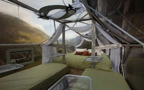 Interior del Skylodge con camas individuales y cortinas, con vista al Valle Sagrado al amanecer