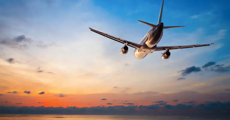 Avión en ascenso contra cielo con tonos naranjas durante atardecer