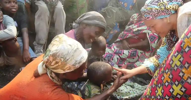 Mujeres y niños en comunidad recibiendo alimentos de persona vistiendo rojo