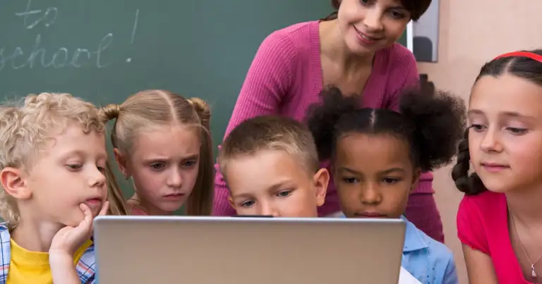 Maestra y niños observando pantalla de computadora portátil en aula escolar