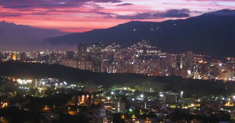 Ciudad durante atardecer rodeada de montañas con iluminación nocturna
