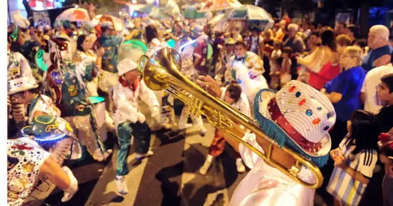 Multitud de personas bailando en desfile de carnaval con disfraces coloridos y sombreros decorados