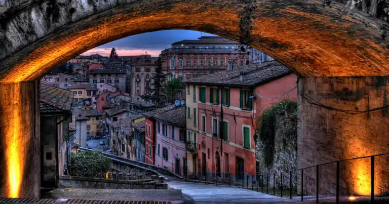 Vista a través de arco de piedra de ciudad italiana con casas coloridas junto a río