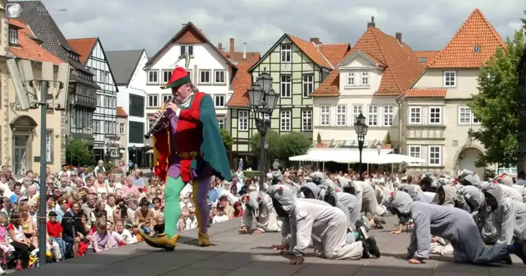 Desfile en plaza de pueblo medieval con marioneta gigante y edificios de arquitectura tradicional