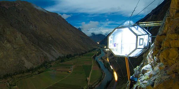 Cápsula transparente del Skylodge iluminada por energía solar colgando sobre el Valle Sagrado al anochecer