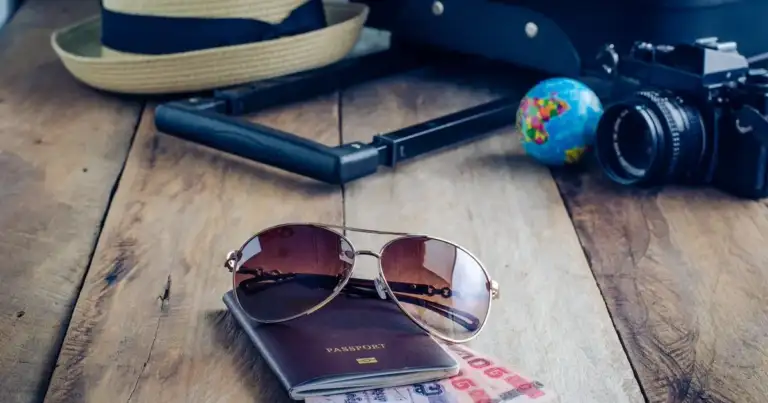 Accesorios de viaje sobre tabla de madera: sombrero, gafas, cámara y documentos