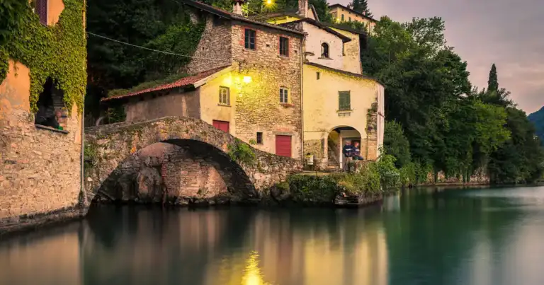 Casa histórica de piedra roja junto a río con puente arqueado