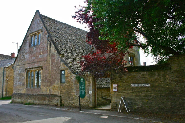 Biblioteca de Bampton, de piedra con techo de pizarra y enredadera, sin la decoración del rodaje