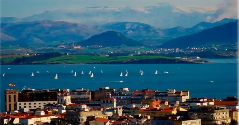 Bahía con embarcaciones junto a ciudad y montañas nevadas al fondo