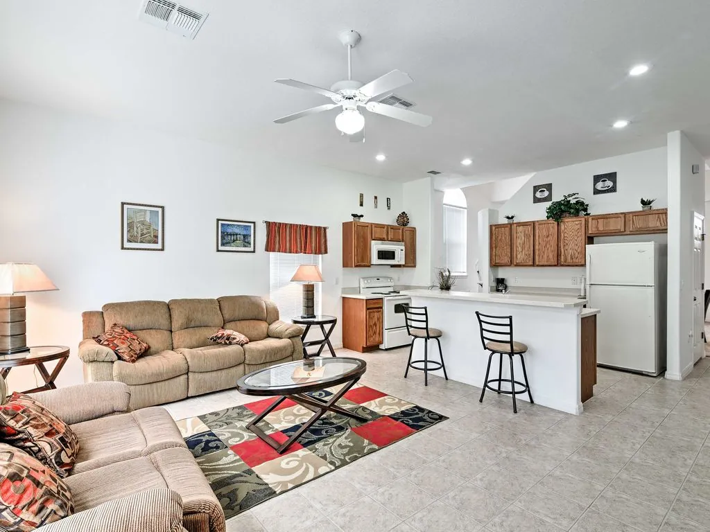 Sala de apartamento vacacional con sofá beige, cocina blanca y alfombra decorada