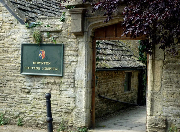 Fachada de piedra con el cartel verde de Downton Cottage Hospital colocado para el rodaje en Bampton