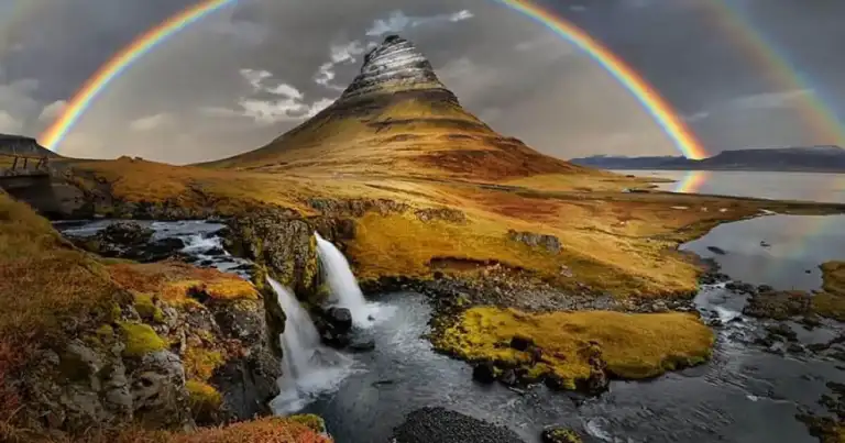 Montaña Kirkjufell en Islandia con cascada y doble arcoíris en el cielo.
