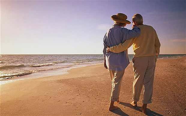 Pareja de jubilados toma de la mano en la playa al atardecer