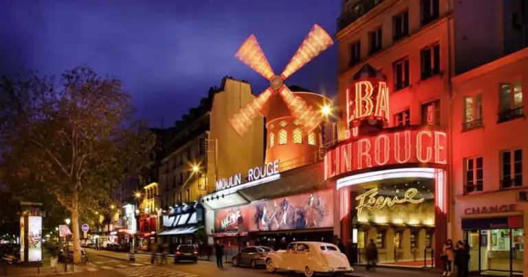 Calle parisina de noche con cabaret de Moulin Rouge y su molino rojo iluminado