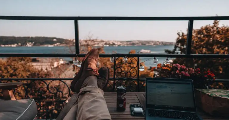 Persona trabajando con una computadora desde un balcón durante un viaje, imagen relacionada con una guía sobre qué es una Working Holiday Visa.
