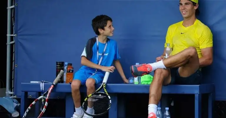 Instructor deportivo en traje amarillo con niño en azul sosteniendo raqueta de tenis