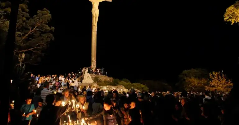 Multitud con velas alrededor de cruz iluminada