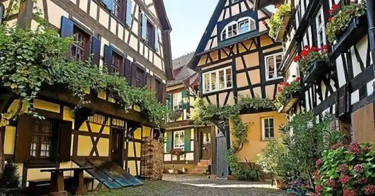 Calle empedrada de pueblo medieval con casas de madera y flores en macetas