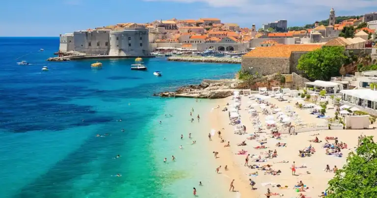 Playa con turistas y ciudad amurallada de piedra al fondo
