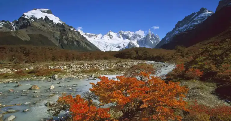 Valle de montañas nevadas con río turquesa fluyendo entre acantilados
