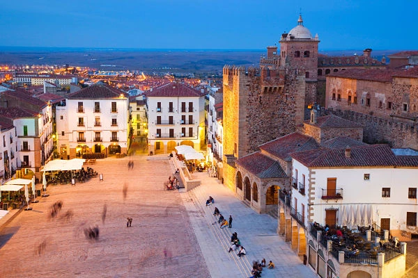 Plaza medieval de Cáceres con edificios de piedra roja y torre fortificada al atardecer