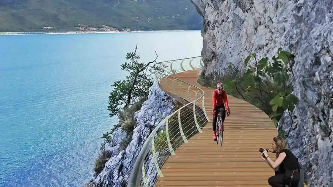Ciclista en bicicleta en pasarela flotante sobre lago rodeado de acantilados