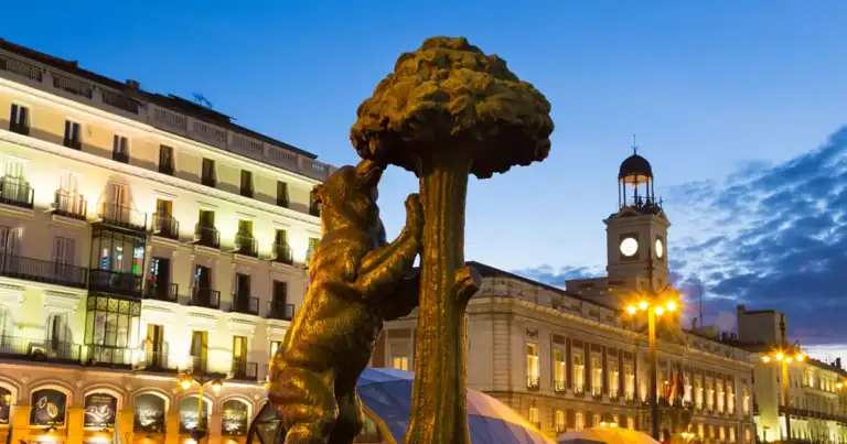 Estatua dorada iluminada de noche rodeada de edificios históricos