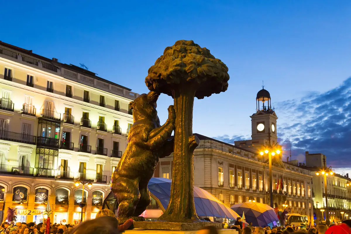 Estatua dorada iluminada de noche rodeada de edificios históricos