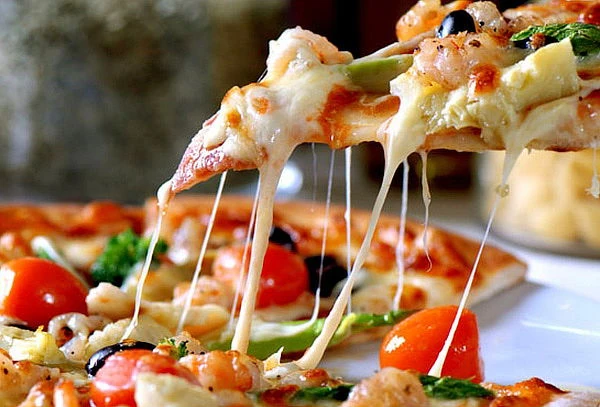 Porciones de pizza con queso hilado y vegetales frescos