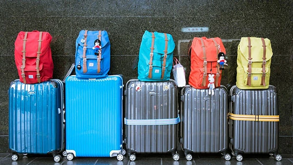 Maletas y mochilas de viaje de colores variados en fila sobre pared gris