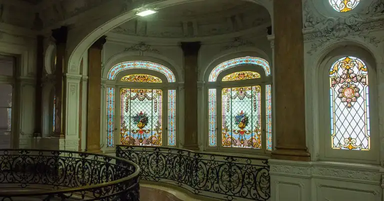 Interior de palacio con vitrales de colores, columnas verdes y barandilla