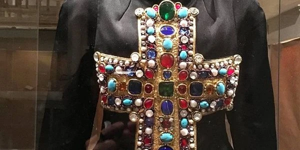 Cruz religiosa adornada con gemas de colores y perlas sobre fondo oscuro